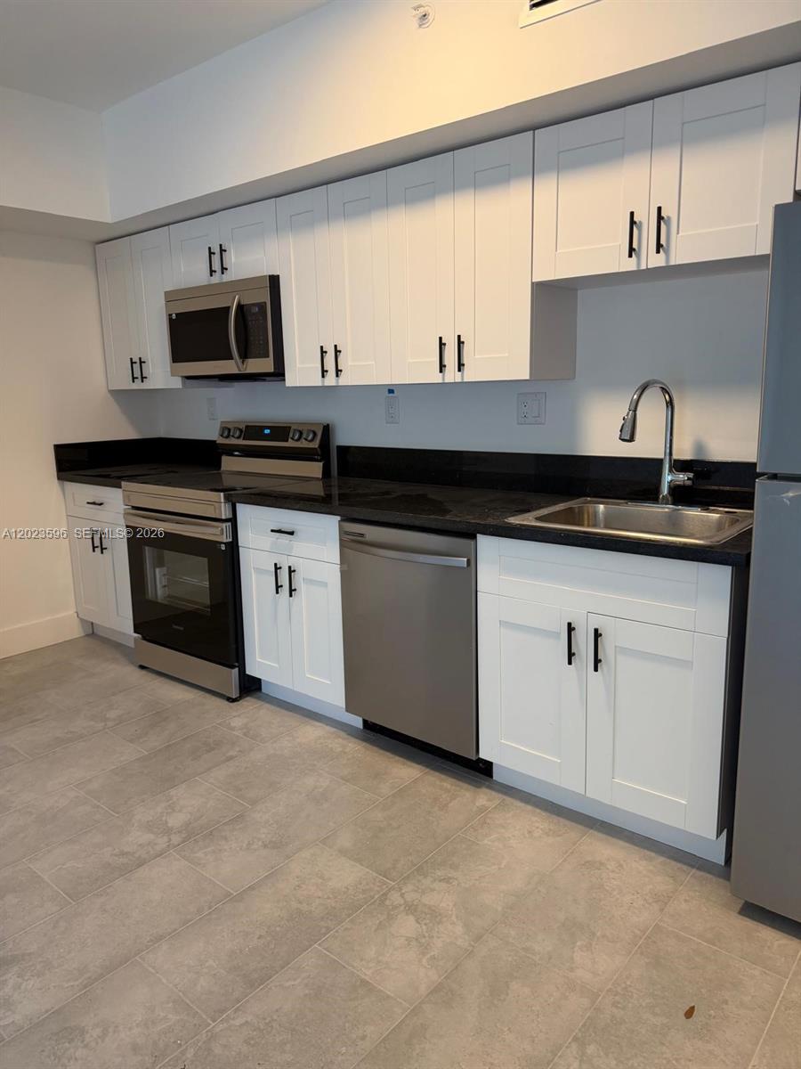 A kitchen features white cabinets, black countertops, stainless steel appliances, and gray tile flooring — 147 Nw 59th St # 301, Miami FL 33127, MIAMI, FL