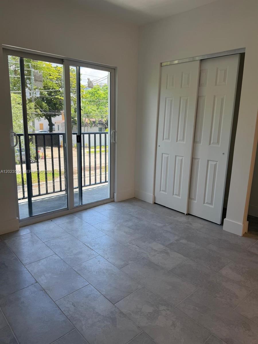 A room with gray tile flooring, a sliding glass door to a balcony, and white closets — 147 Nw 59th St # 301, Miami FL 33127, MIAMI, FL
