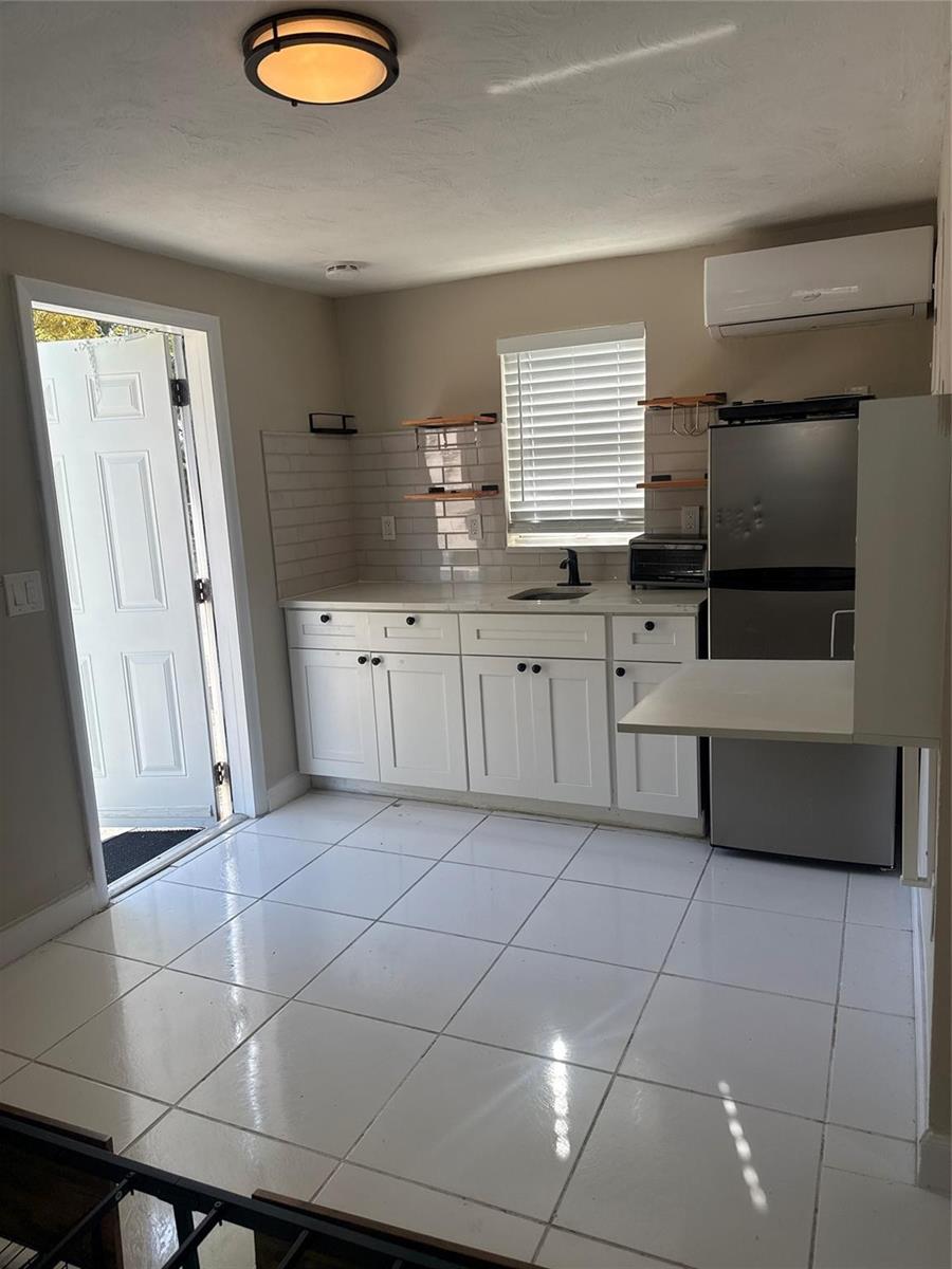 A small kitchen features white cabinets, a stainless steel refrigerator, tile flooring, and a door — 299 SE 12th Avenue, Deerfield Beach FL 33441, DEERFIELD BEACH, FL