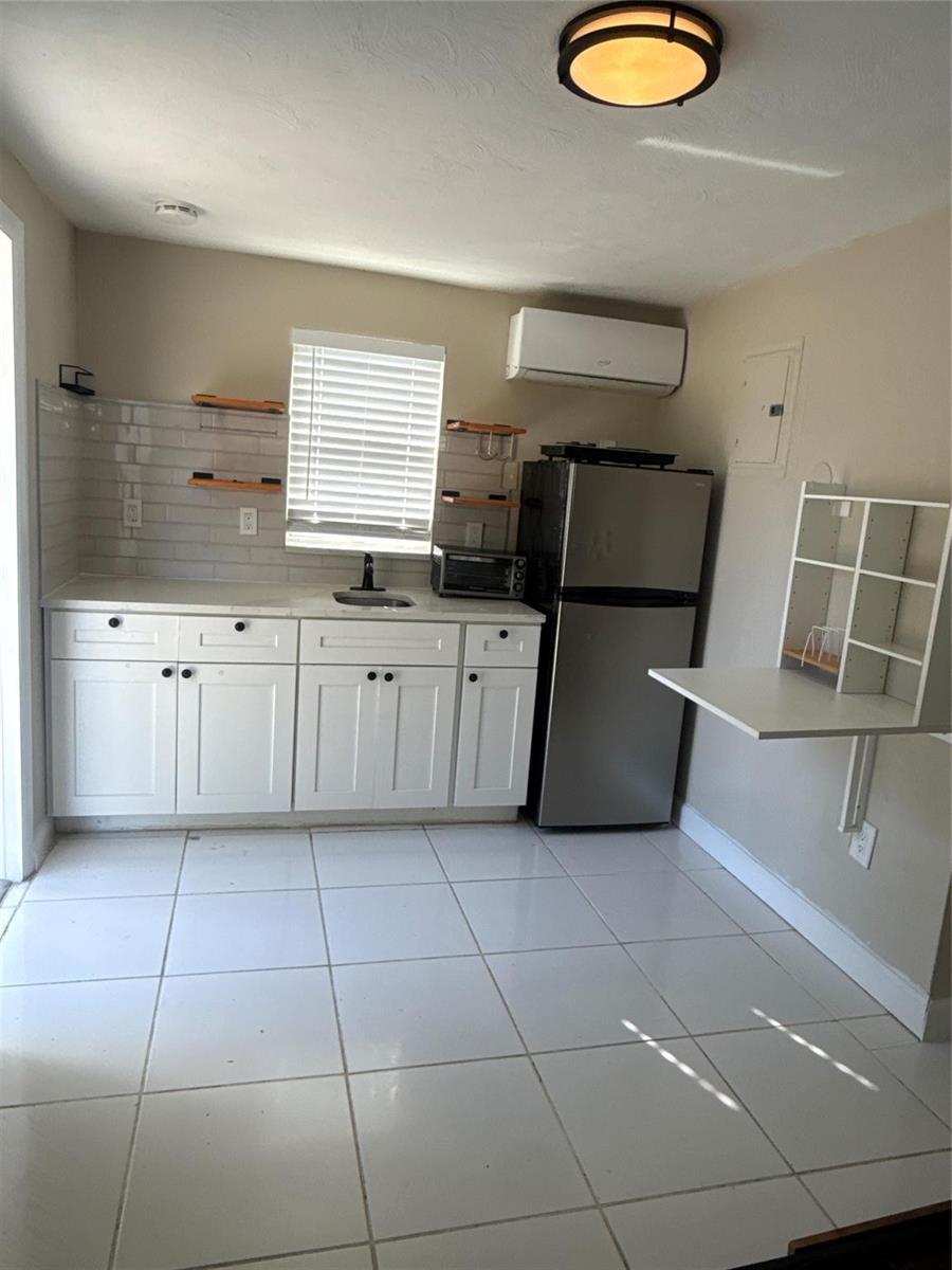A small kitchen features white cabinets, a stainless steel refrigerator, and a wall-mounted folding table — 299 SE 12th Avenue, Deerfield Beach FL 33441, DEERFIELD BEACH, FL