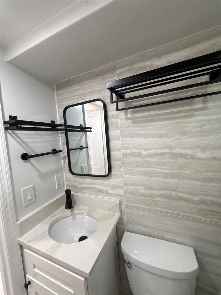 A small bathroom features a white vanity, a black-framed mirror, and black wall-mounted shelves — 299 SE 12th Avenue, Deerfield Beach FL 33441, DEERFIELD BEACH, FL