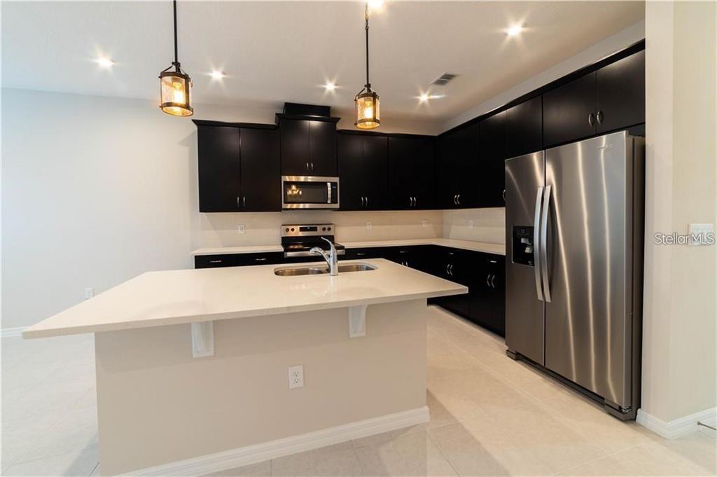 A kitchen features dark cabinets, stainless steel appliances, and a central island with a countertop — 16306 PRAIRIE SCHOOL DRIVE, WINTER GARDEN, FL