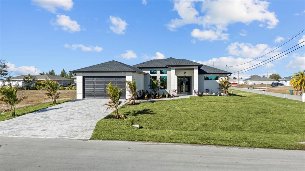 A modern single-story house with a gray garage, paved driveway, and a manicured lawn — 1030 NE 2ND AVENUE, CAPE CORAL, FL
