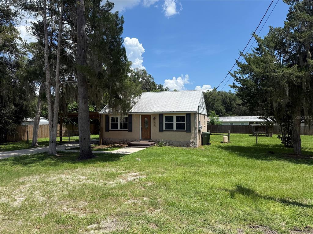A small, single-story house with a metal roof sits on a grassy lot with trees — 937 COUNTY ROAD 481W, LAKE PANASOFFKEE, FL