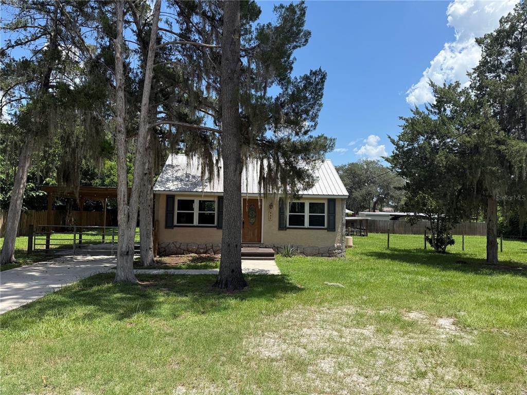 A small, single-story house with a metal roof and stone foundation sits on a grassy lot — 937 COUNTY ROAD 481W, LAKE PANASOFFKEE, FL