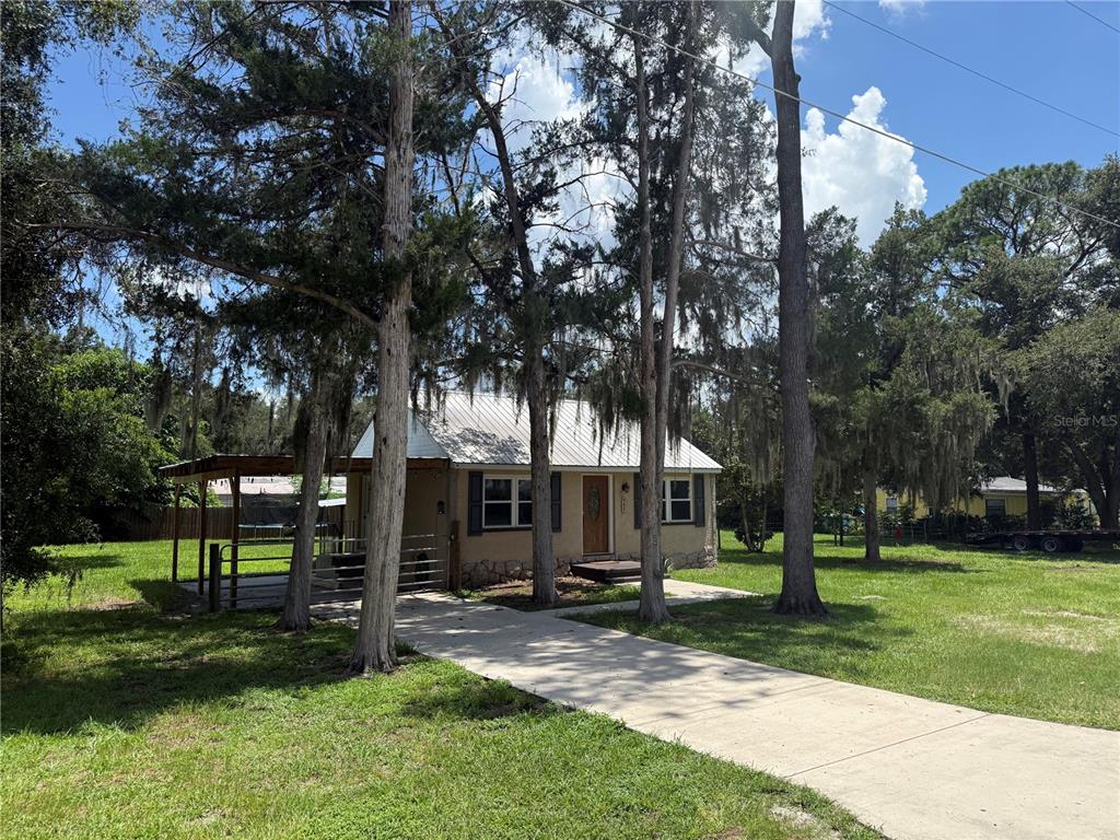 A single-story house with a metal roof and a carport sits on a grassy lot — 937 COUNTY ROAD 481W, LAKE PANASOFFKEE, FL