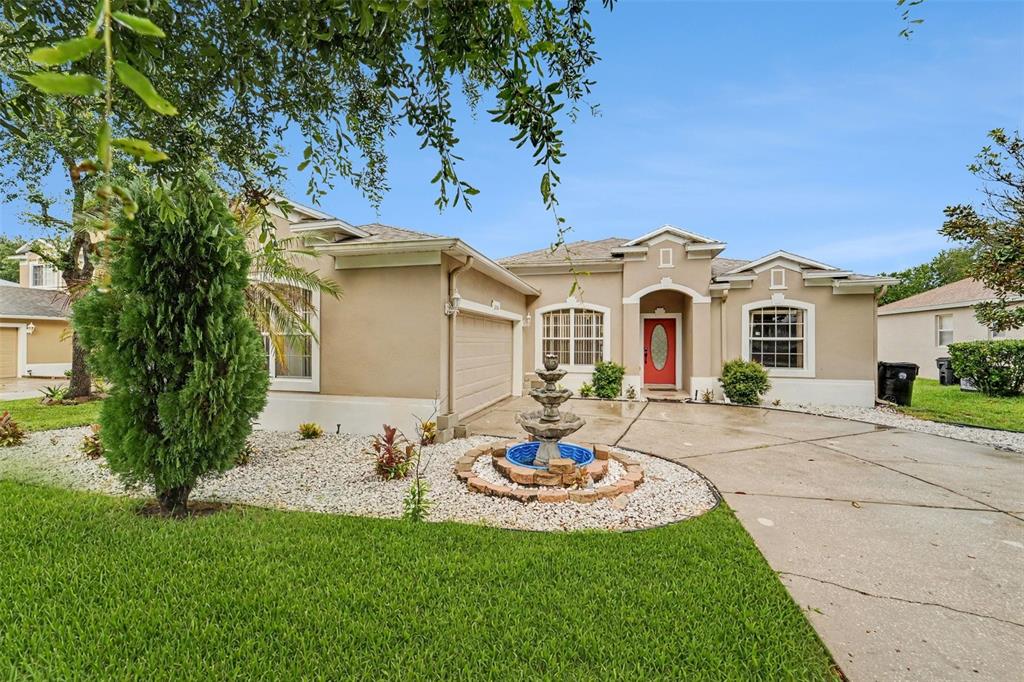 A single-story tan house with a red front door, a fountain, and a concrete driveway — 2056 CLAPPER TRAIL, APOPKA, FL