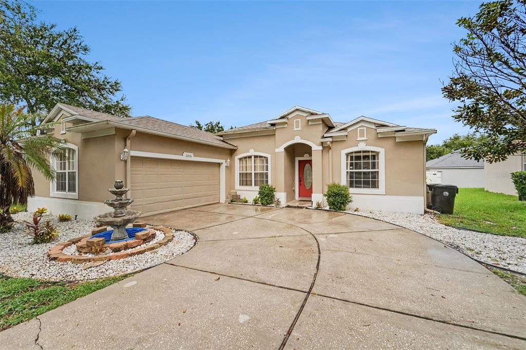 A single-story tan house with a red front door, two-car garage, and a front fountain — 2056 CLAPPER TRAIL, APOPKA, FL