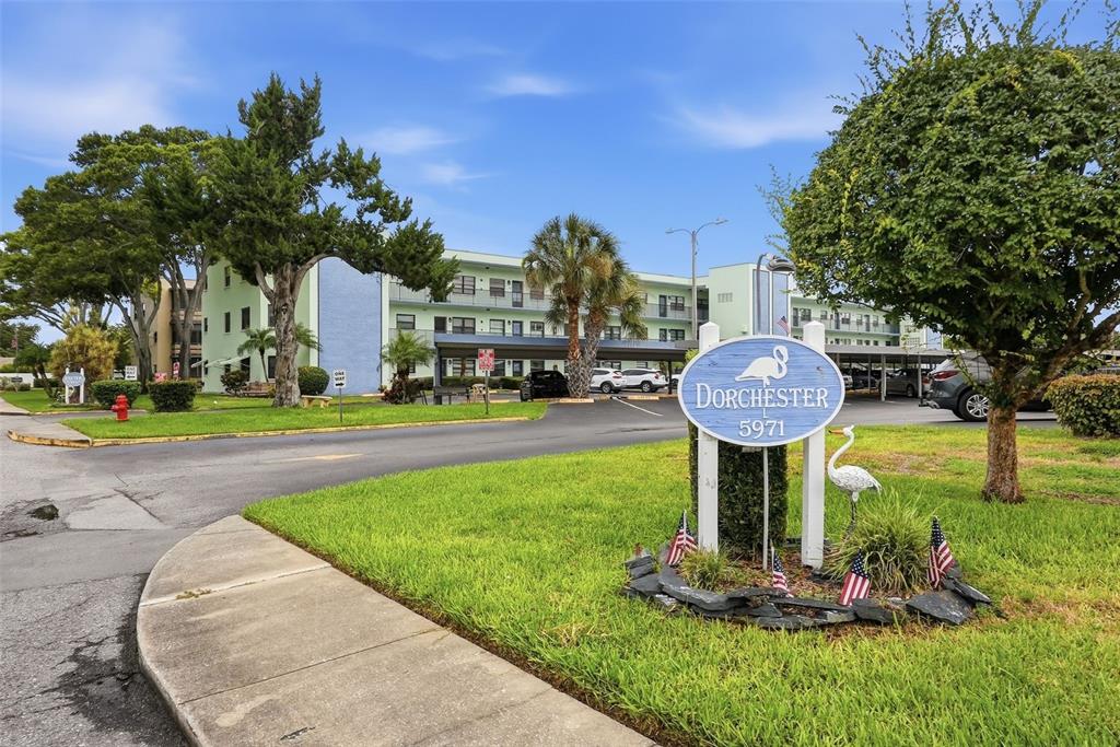An outdoor walkway features a light green brick wall, an elevator, and a seating area — 5973 TERRACE PARK DRIVE N UNIT 109, ST PETERSBURG, FL