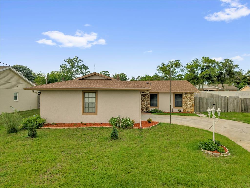 A single-story house with a tan stucco exterior, stone accents, and a brown shingled roof — 46 LANTANA DRIVE, DEBARY, FL