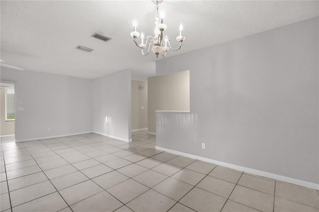 An open-concept dining area features light-colored tile flooring, gray walls, and a decorative chandelier — 46 LANTANA DRIVE, DEBARY, FL