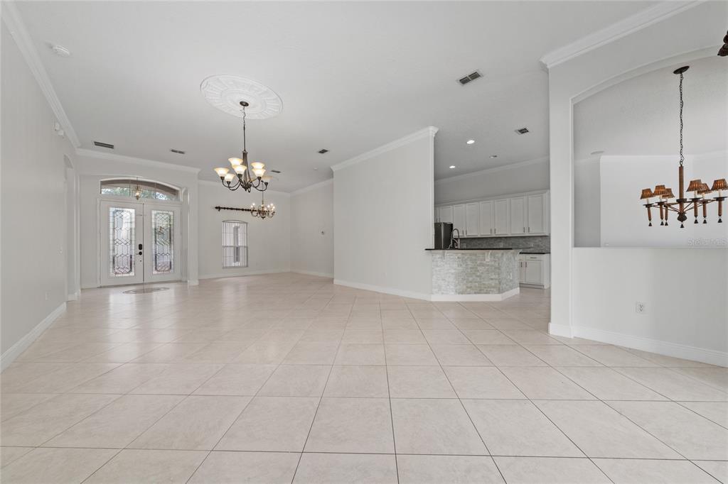 An open-concept living area features light tile flooring, white walls, and two decorative chandeliers — 3540 VALLEYVIEW DR, KISSIMMEE, FL