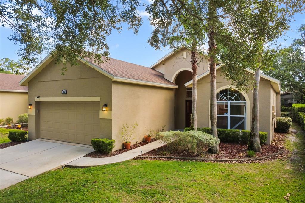 A tan single-story house with a two-car garage, arched entryway, and a large front window — 1154 KERSFIELD CIRCLE, LAKE MARY, FL