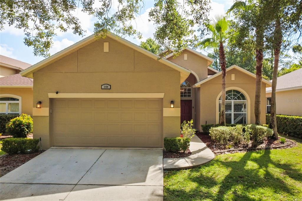 A tan single-story house with a two-car garage, arched window, and a concrete driveway — 1154 KERSFIELD CIRCLE, LAKE MARY, FL