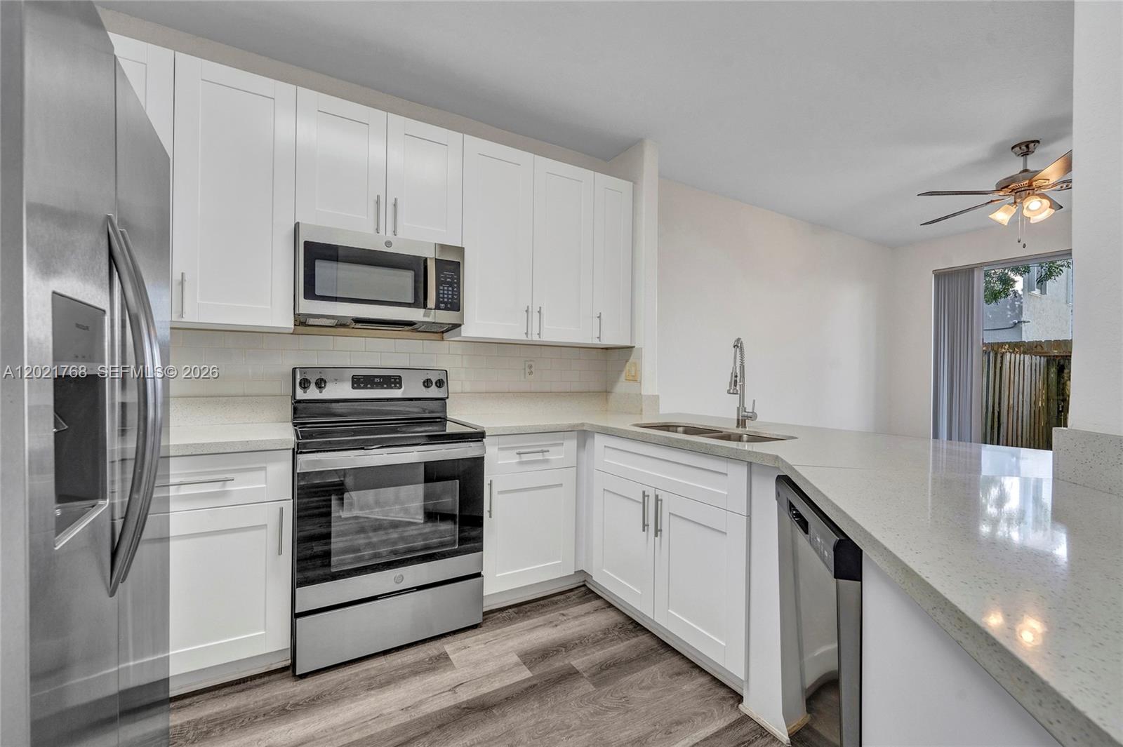 A kitchen features white cabinets, stainless steel appliances, and light countertops over wood-look flooring — 1445 SE 24th Rd, Homestead FL 33035, HOMESTEAD, FL