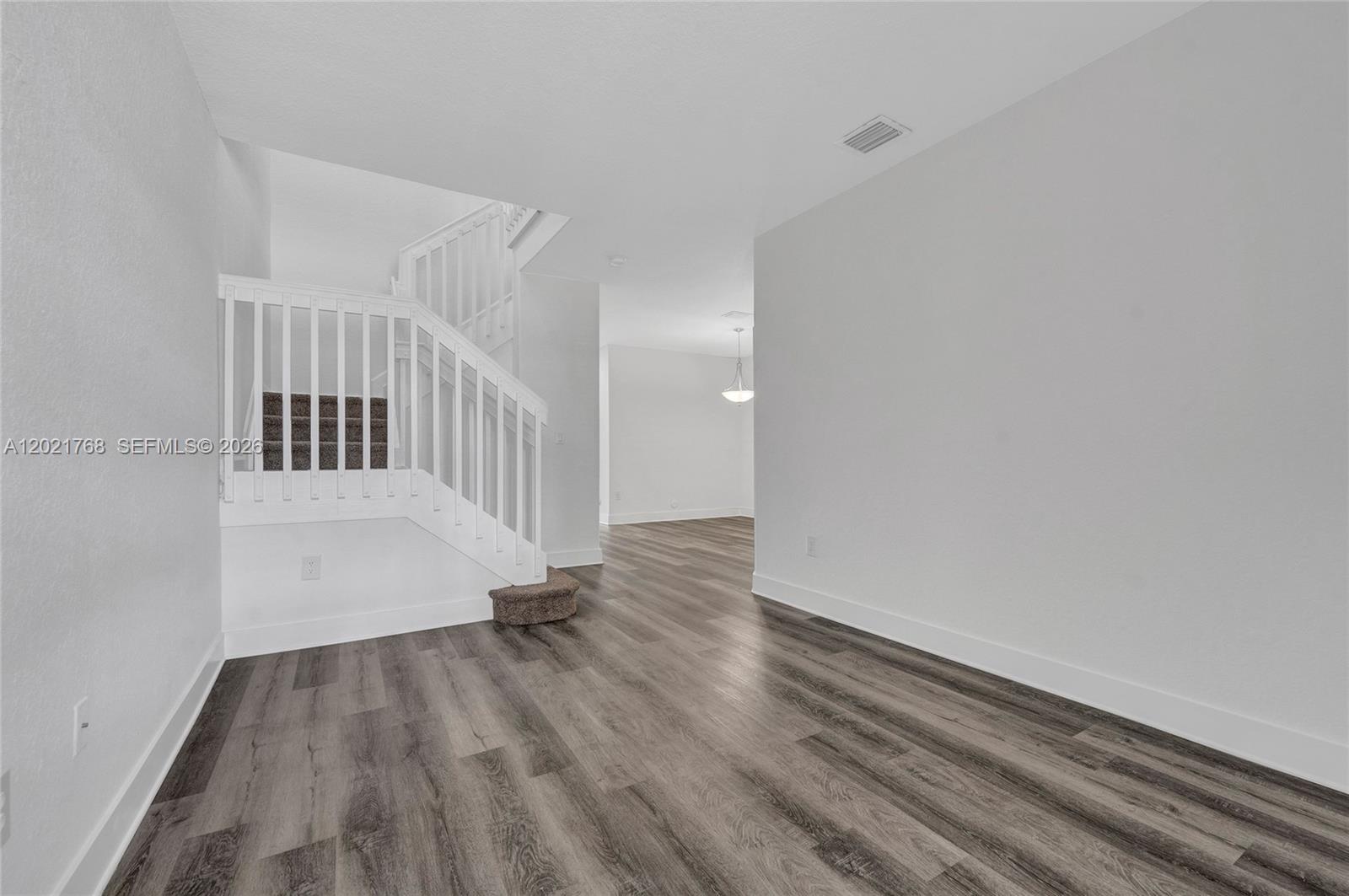 An interior view shows a room with wood-look flooring, white walls, and a staircase — 1445 SE 24th Rd, Homestead FL 33035, HOMESTEAD, FL