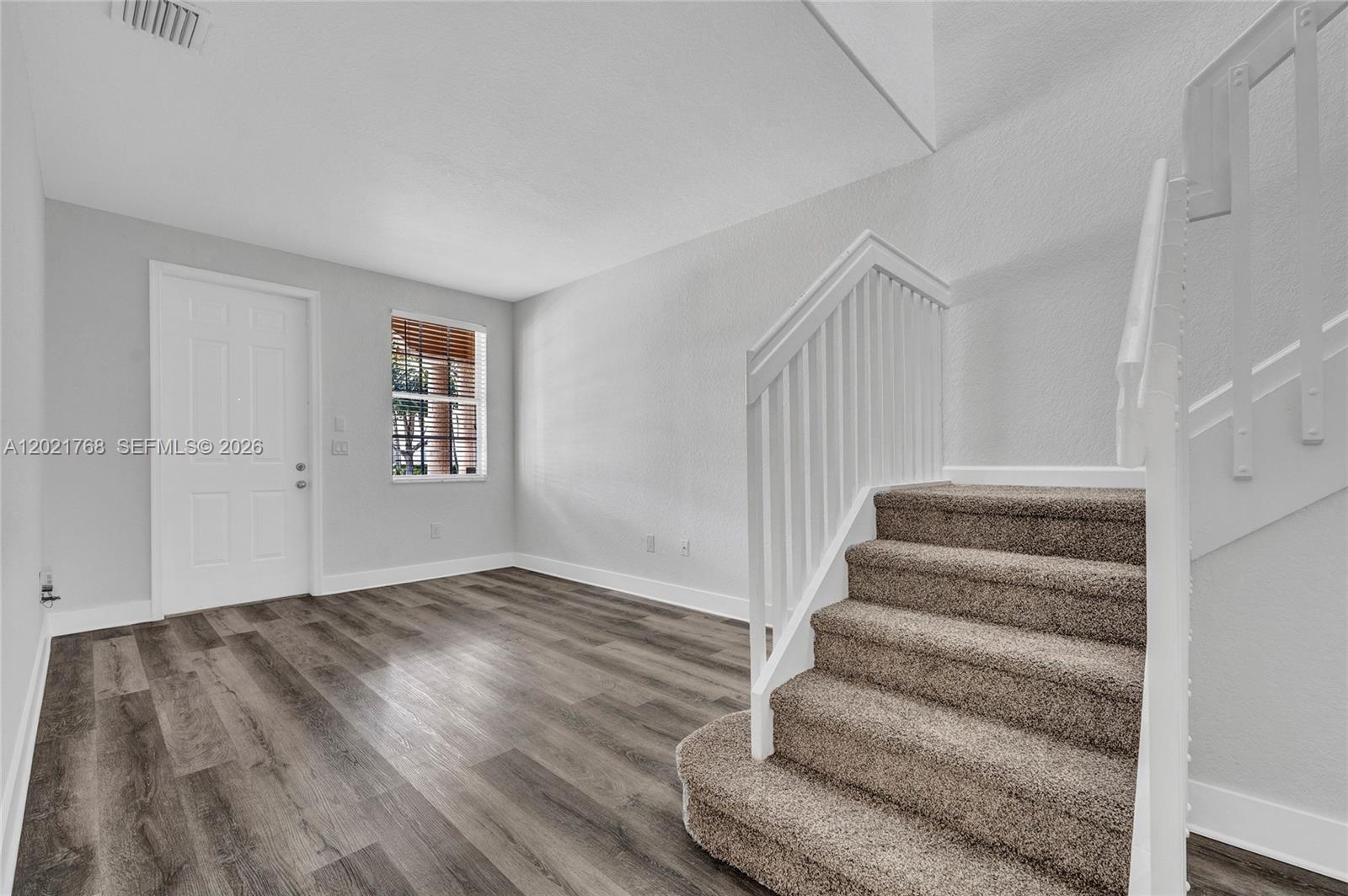 A room with wood-look flooring, a white door, a window, and carpeted stairs — 1445 SE 24th Rd, Homestead FL 33035, HOMESTEAD, FL