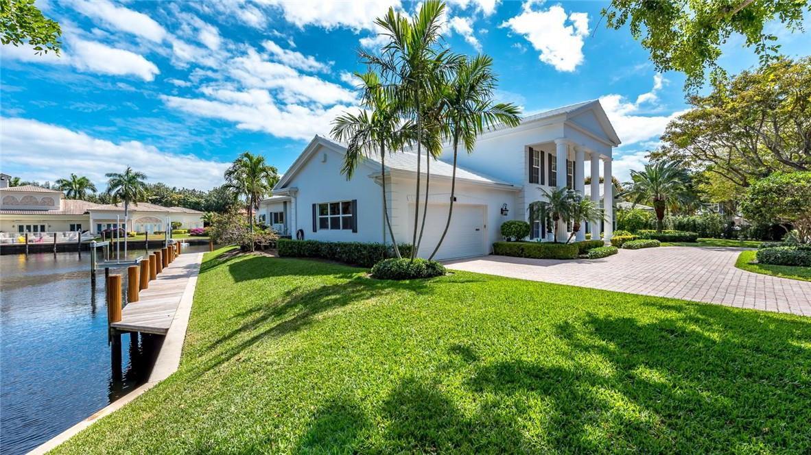 A white two-story house with a paved driveway, palm trees, and a wooden dock on water — 2 Compass Lane, Fort Lauderdale FL 33308, FORT LAUDERDALE, FL