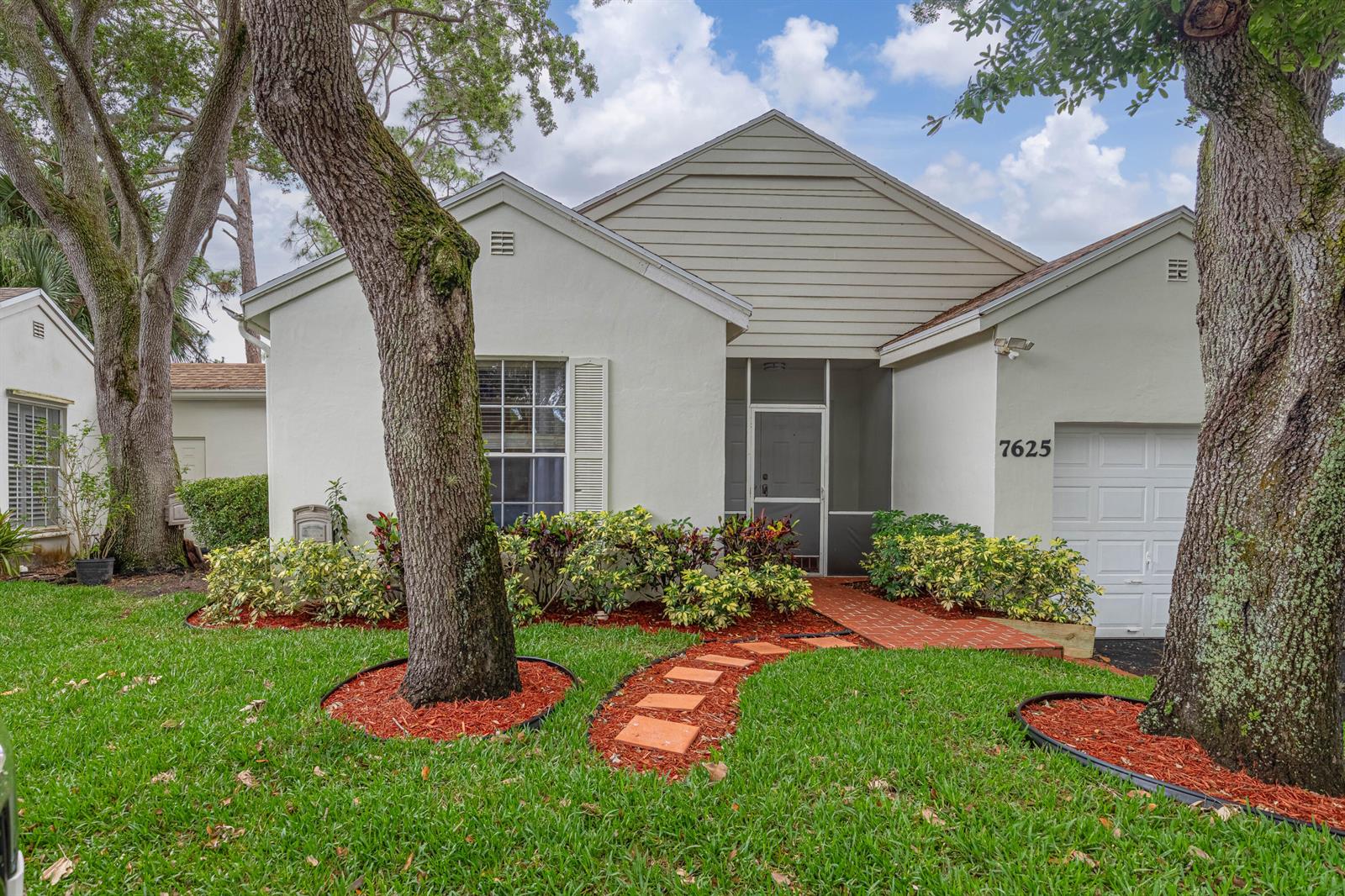 A single-story house features a white stucco exterior, a screened entryway, and a brick walkway — 7625 Forest Green Lane, Boynton Beach FL 33436, BOYNTON BEACH, FL