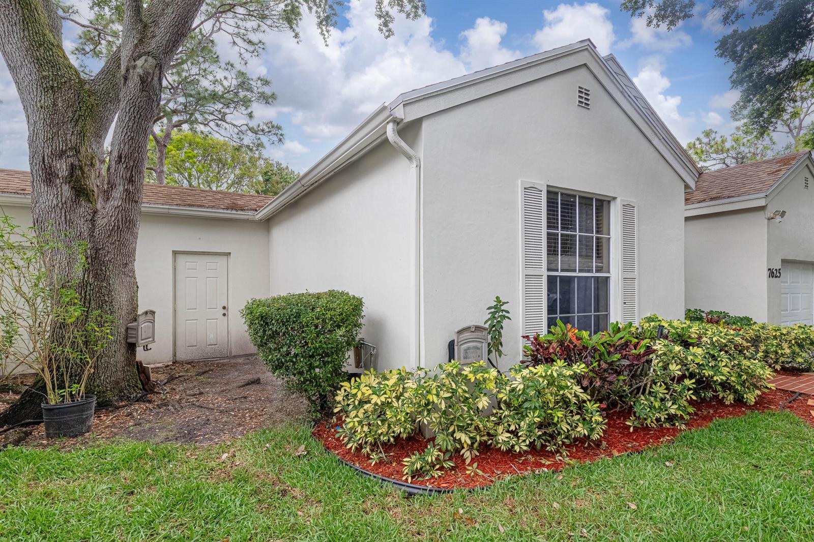 A white stucco house exterior features a front door, a window with shutters, and landscaping — 7625 Forest Green Lane, Boynton Beach FL 33436, BOYNTON BEACH, FL