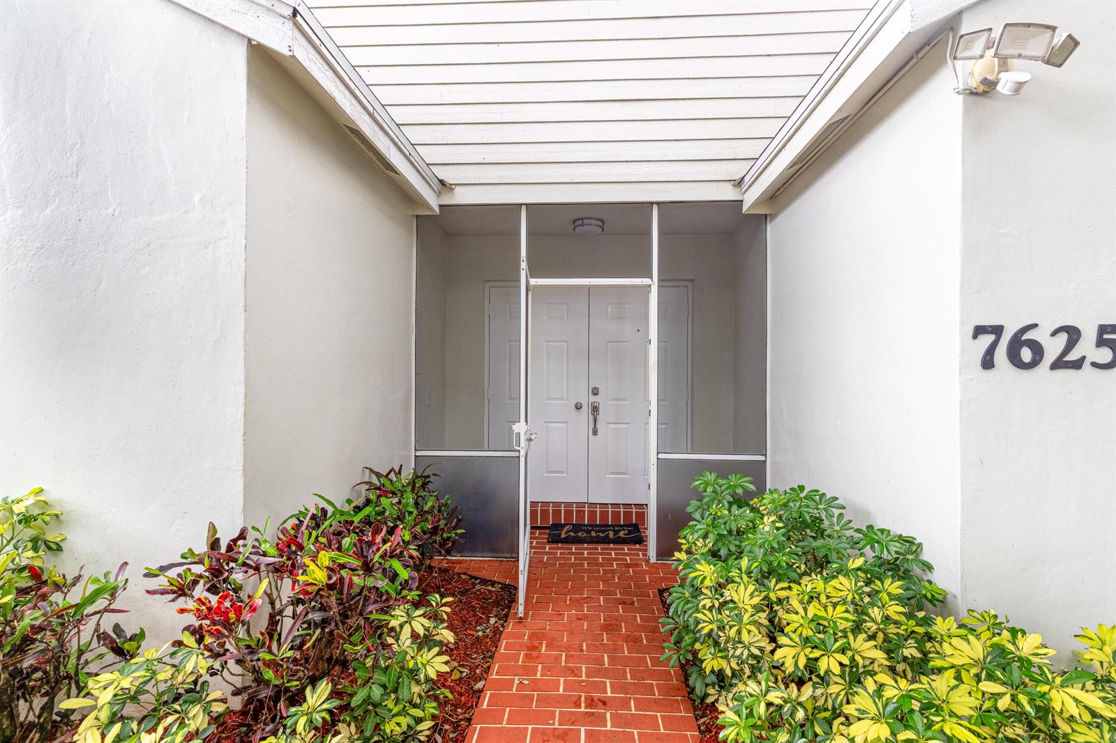 A brick walkway leads to a screened entryway with double doors and surrounding landscaping — 7625 Forest Green Lane, Boynton Beach FL 33436, BOYNTON BEACH, FL