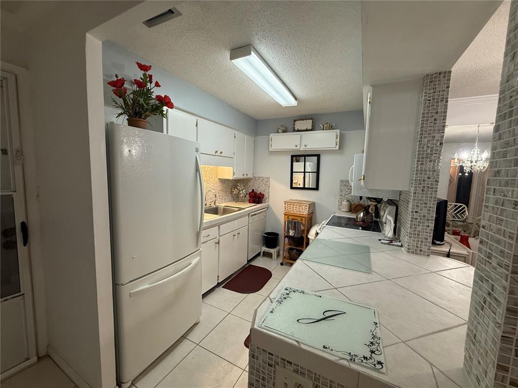 A galley-style kitchen features white cabinets, tiled countertops, and a white refrigerator — 125 PICARDY VILLA CIRCLE UNIT 101, BRANDON, FL
