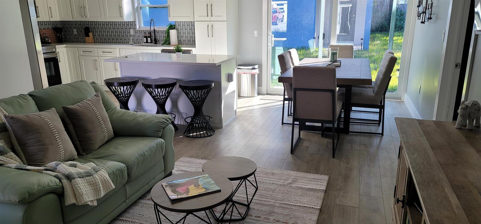 An open-concept kitchen, dining area, and living room with light wood floors and white cabinetry — 106 E Chandler Road, Cloud Lake FL 33406, CLOUD LAKE, FL