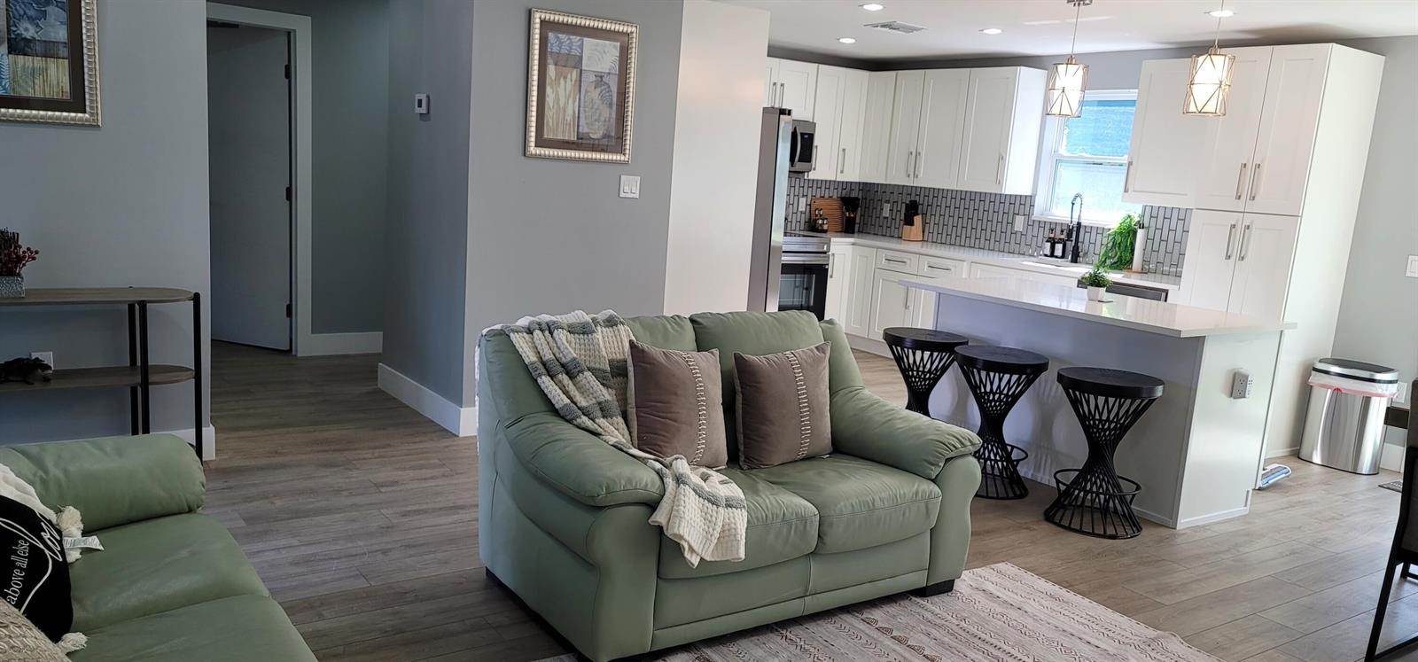 A living room with a green sofa opens into a kitchen featuring white cabinets — 106 E Chandler Road, Cloud Lake FL 33406, CLOUD LAKE, FL