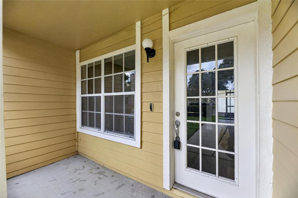 A covered porch with yellow horizontal siding, a white-framed window, and a glass-paned door — 1214 BIG PINE DRIVE, VALRICO, FL