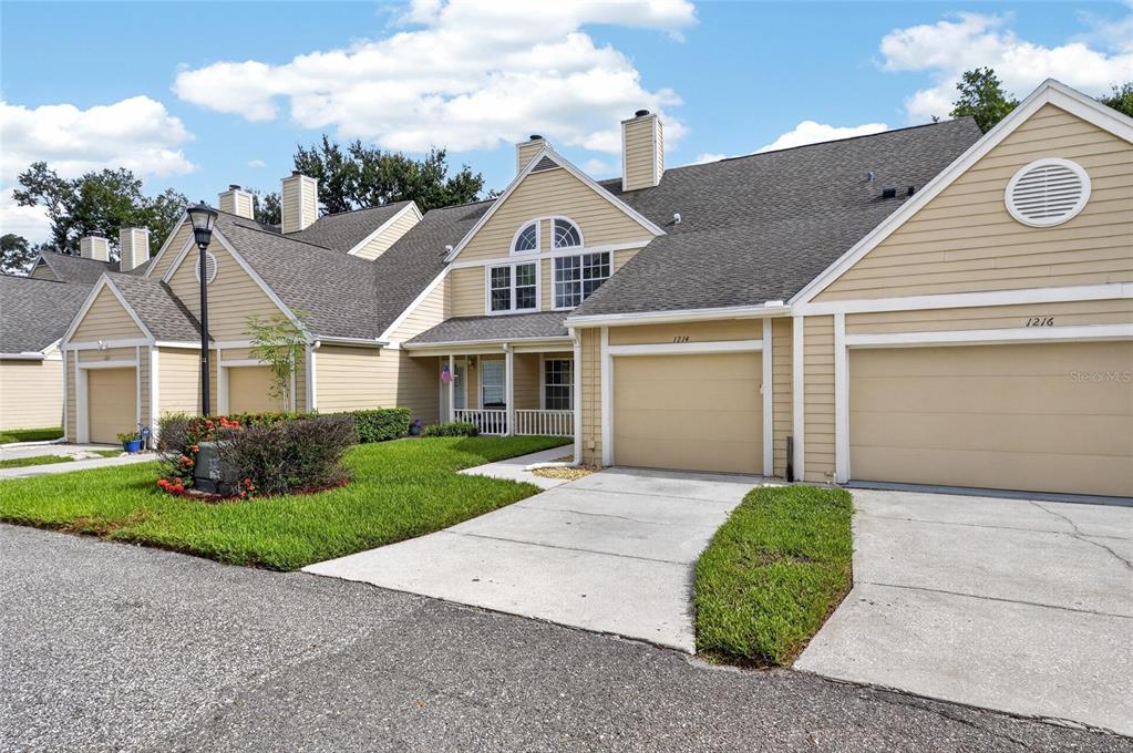 A row of tan townhouses features attached garages, gray shingled roofs, and a shared lawn — 1214 BIG PINE DRIVE, VALRICO, FL