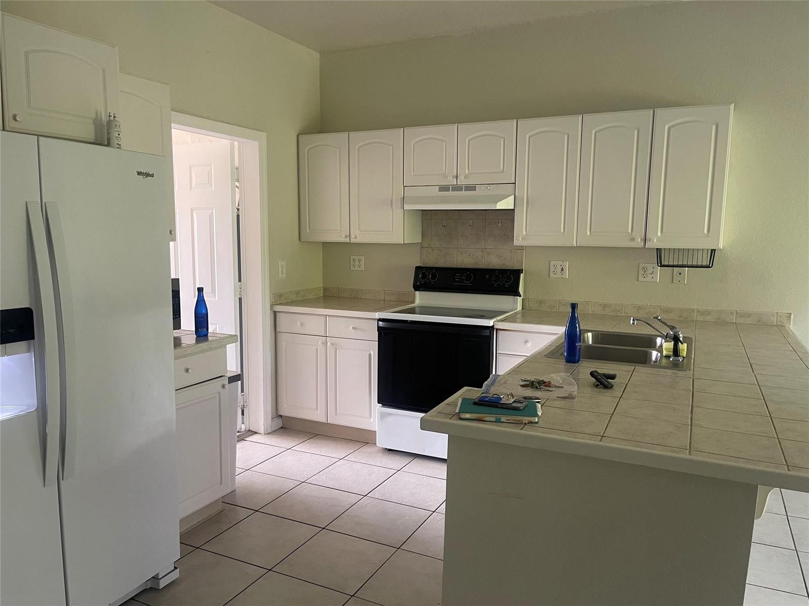 A kitchen features white cabinets, a black stove, a tiled countertop, and light-colored floor tiles — 717 NE 4th Street, Hallandale Beach FL 33009, HALLANDALE BEACH, FL