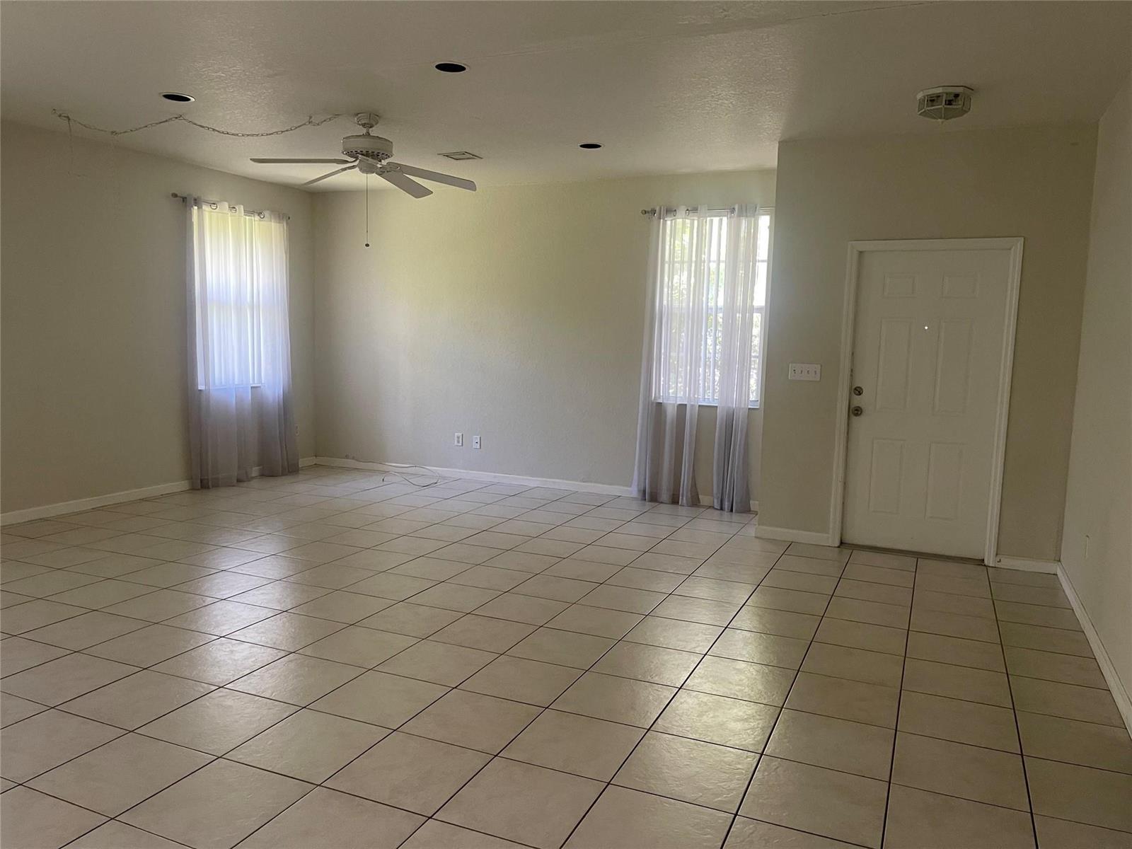 An empty living room features light-colored tile floors, a ceiling fan, and two windows — 717 NE 4th Street, Hallandale Beach FL 33009, HALLANDALE BEACH, FL