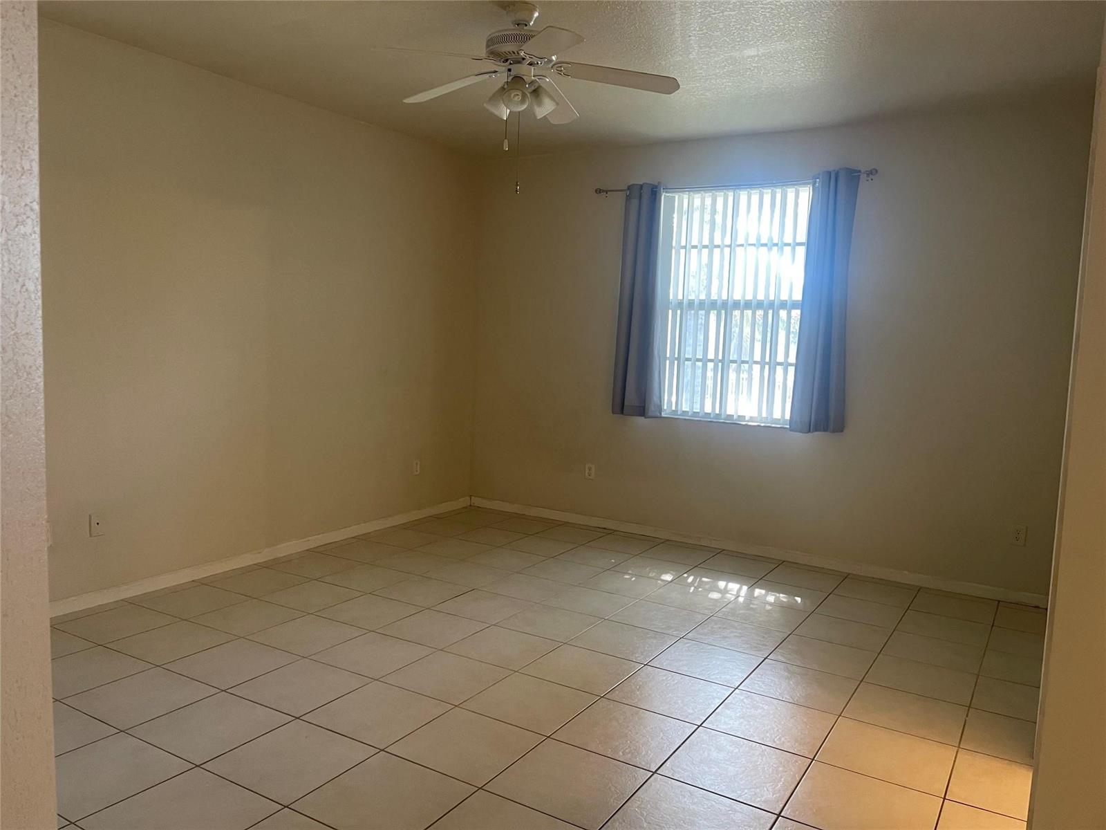 An empty room features beige walls, light-colored floor tiles, a ceiling fan, and a window — 717 NE 4th Street, Hallandale Beach FL 33009, HALLANDALE BEACH, FL