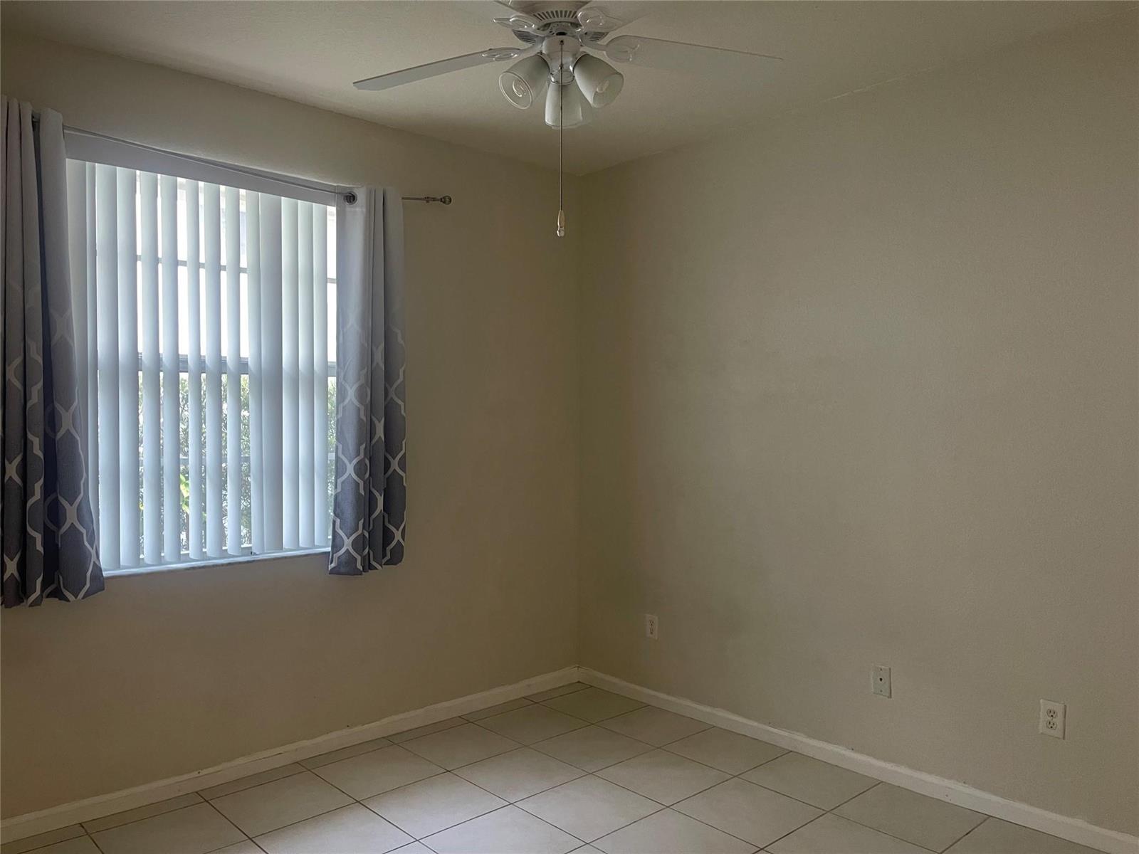 An empty bedroom features light-colored tile flooring, a ceiling fan, and a window with curtains — 717 NE 4th Street, Hallandale Beach FL 33009, HALLANDALE BEACH, FL