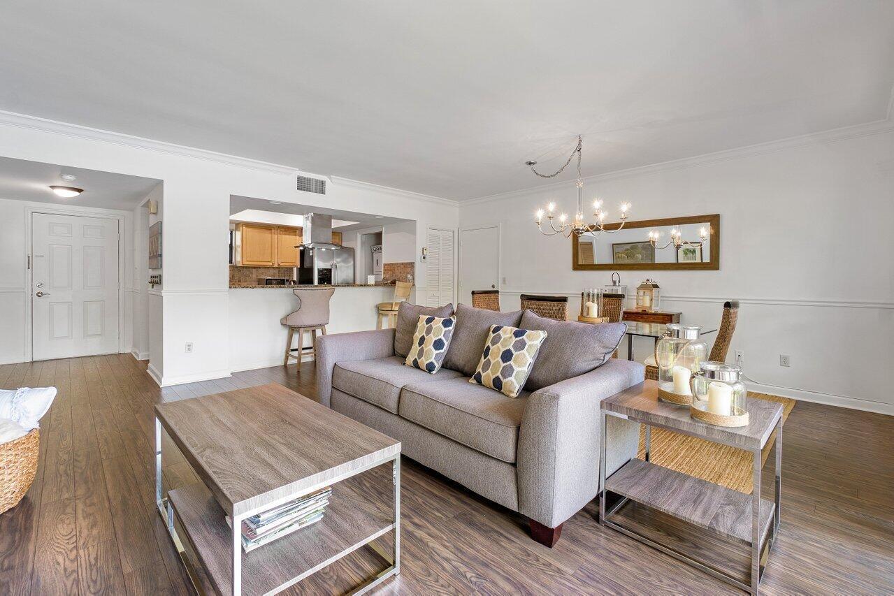 A living room with a gray sofa, wood coffee table, and an open kitchen area — 11863 Wimbledon Circle # 433, Wellington FL 33414, WELLINGTON, FL