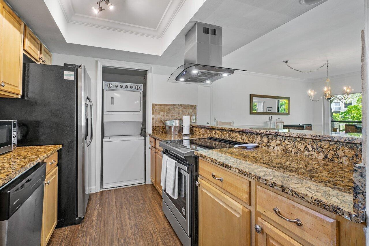 A kitchen features wood cabinets, granite countertops, stainless steel appliances, and a stacked laundry unit — 11863 Wimbledon Circle # 433, Wellington FL 33414, WELLINGTON, FL