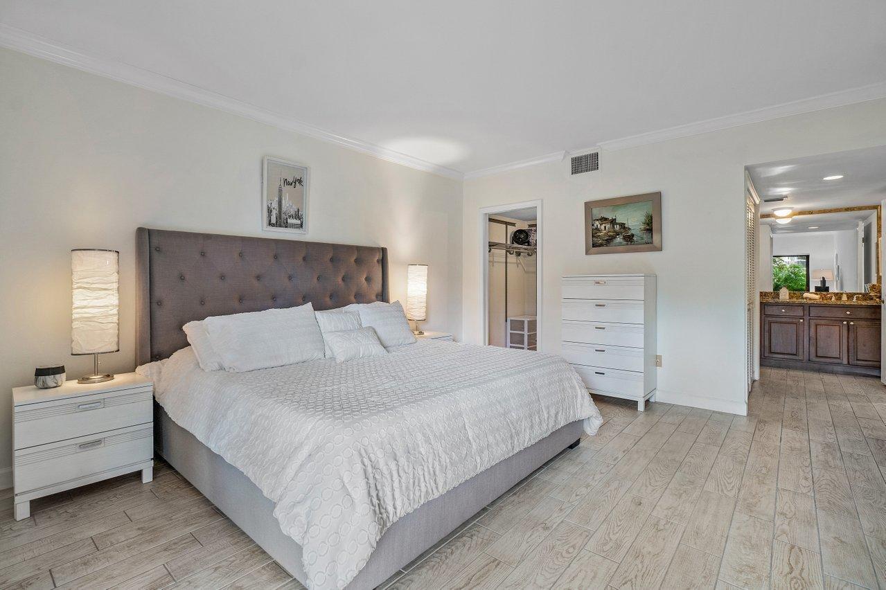 A bedroom features a gray tufted headboard, white bedding, a dresser, and light wood-look flooring — 11863 Wimbledon Circle # 433, Wellington FL 33414, WELLINGTON, FL