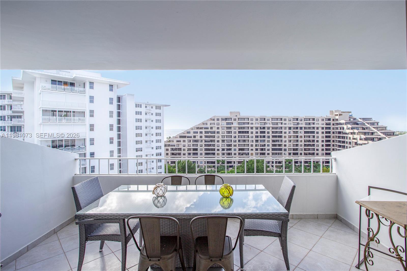 A balcony features a glass-topped dining table with chairs overlooking nearby apartment buildings — 199 Ocean Lane Dr # 1207, Key Biscayne FL 33149, KEY BISCAYNE, FL