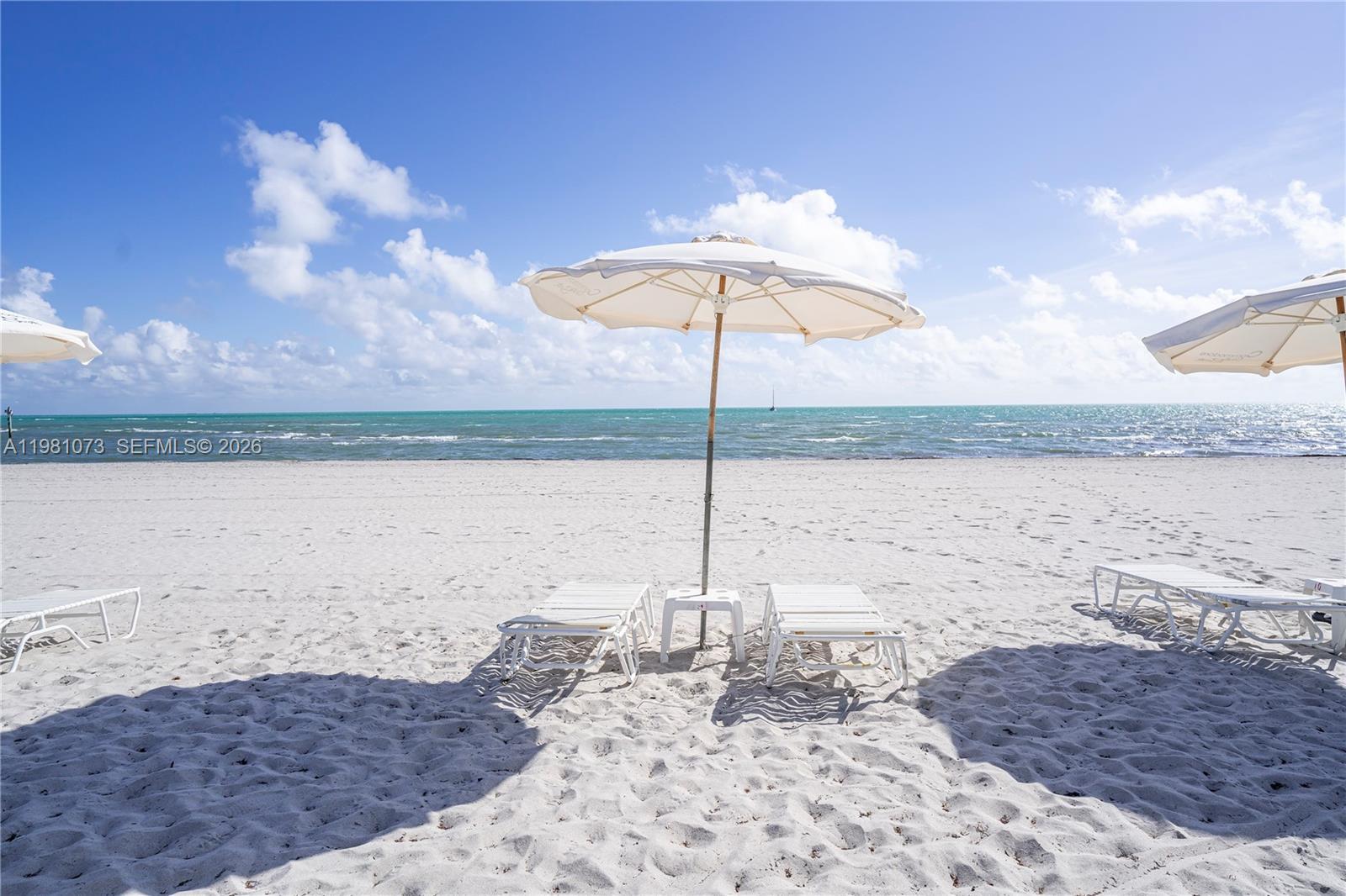 White beach umbrellas and lounge chairs sit on a sandy beach overlooking the ocean — 199 Ocean Lane Dr # 1207, Key Biscayne FL 33149, KEY BISCAYNE, FL