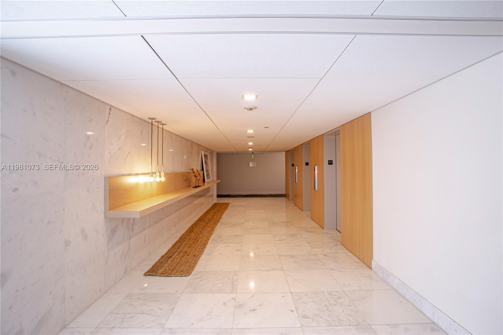 A modern hallway features marble floors, wood paneling, a floating shelf, and elevator doors — 199 Ocean Lane Dr # 1207, Key Biscayne FL 33149, KEY BISCAYNE, FL
