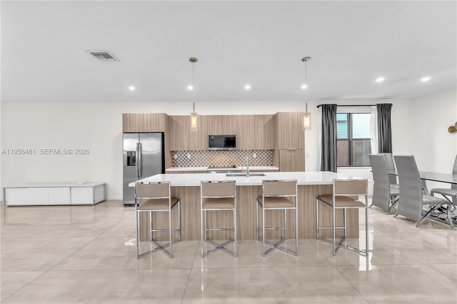 A modern kitchen features light wood cabinetry, a large white island, and four bar stools — 10250 NW 76th Ter, Doral FL 33178, DORAL, FL
