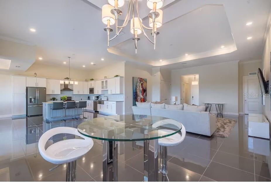 An open-concept kitchen and living area features white cabinetry, a glass table, and tile flooring — 4731 CLOCK TOWER DRIVE UNIT 401, KISSIMMEE, FL