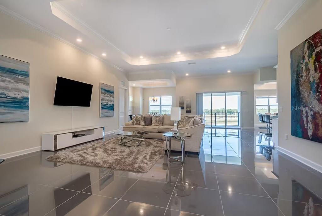 A spacious living room features glossy tile floors, a tray ceiling, and a neutral sofa — 4731 CLOCK TOWER DRIVE UNIT 401, KISSIMMEE, FL