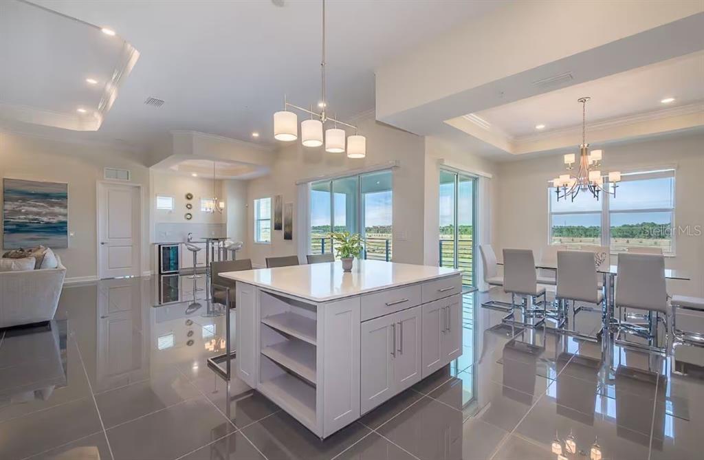 A modern kitchen features a large white island, gray tile floors, and an adjacent dining area — 4731 CLOCK TOWER DRIVE UNIT 401, KISSIMMEE, FL
