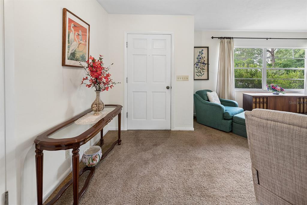 A carpeted living room features a wooden console table, a white door, and a teal armchair — 6267 CLANCE ROAD, KEYSTONE HEIGHTS, FL