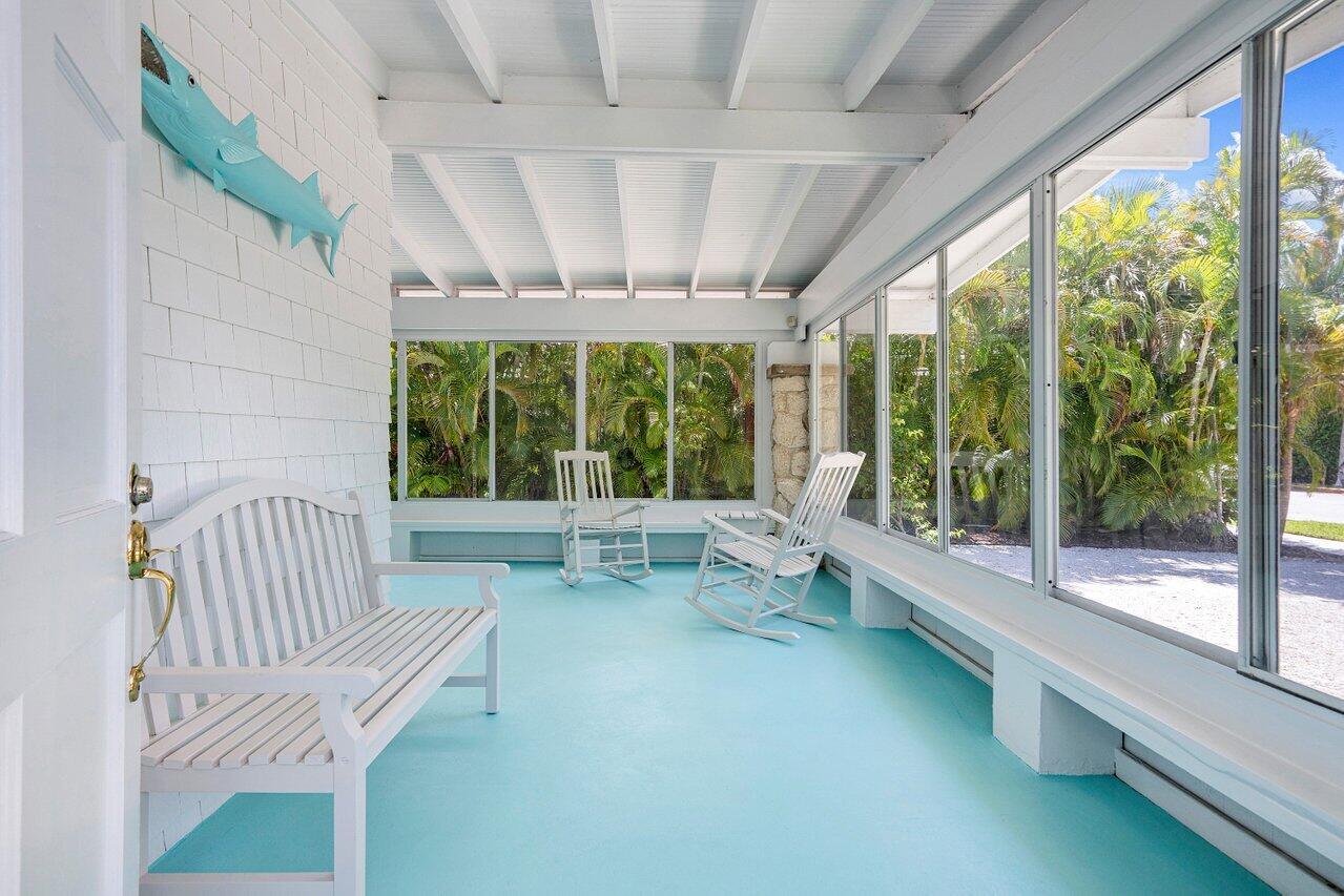 A sunroom with a light blue floor, white furniture, and large windows overlooking palm trees — 141 Chilean Avenue, Palm Beach FL 33480, PALM BEACH, FL