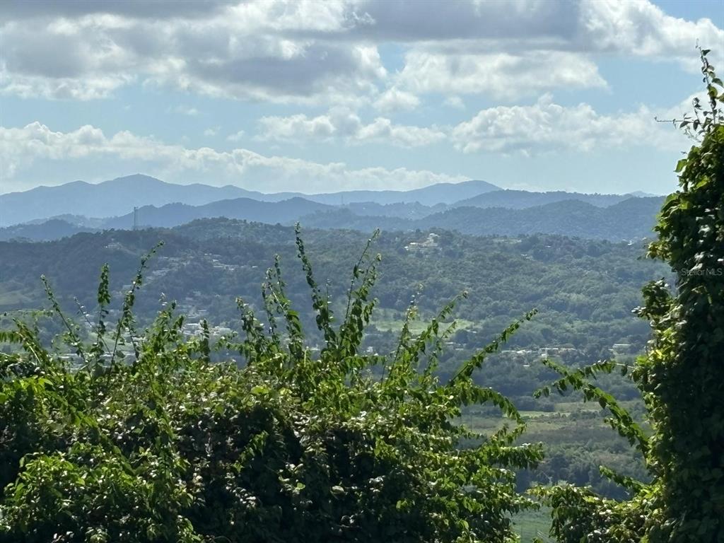 A scenic view of rolling green hills and mountains under a cloudy blue sky — 31 INT 950 KM.HM 9.7 BO RIO BLANCO, NAGUABO, PR
