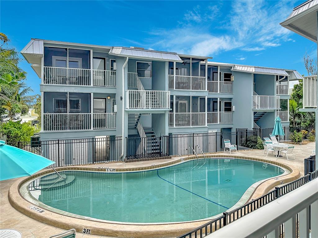 A multi-story apartment building overlooks a swimming pool with a fenced patio area — 205 HIGHLAND AVENUE UNIT 3, BRADENTON BEACH, FL