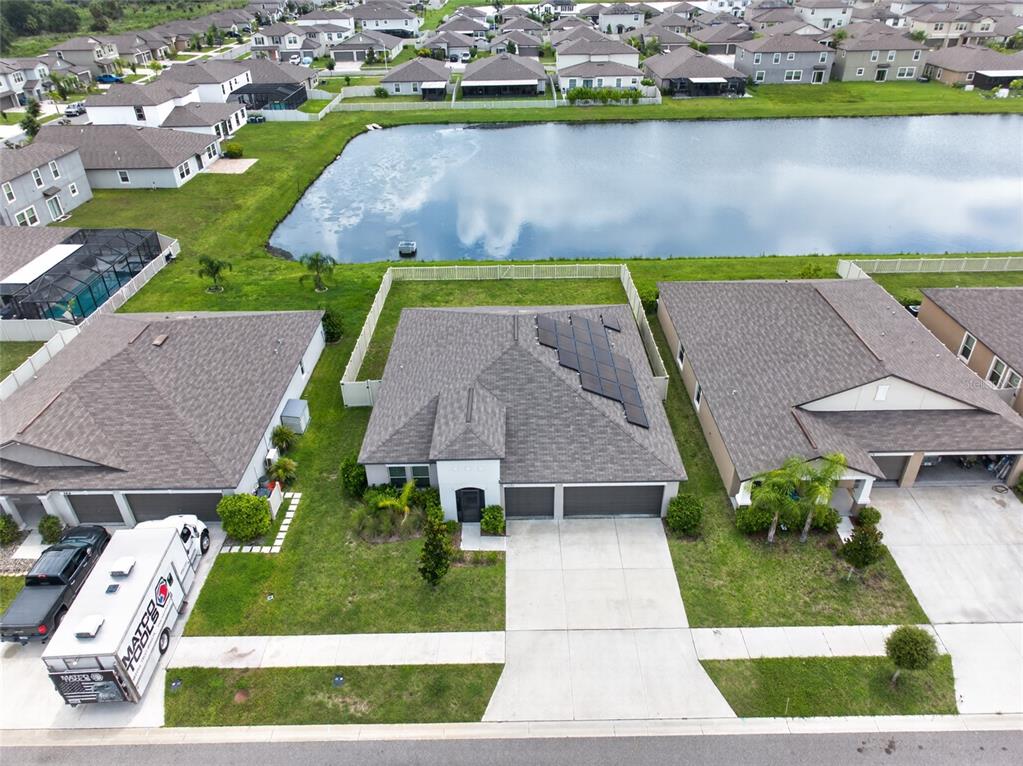 An aerial view shows a suburban house with solar panels on the roof near a pond — 5420 LESLIE CANYON DRIVE, WIMAUMA, FL