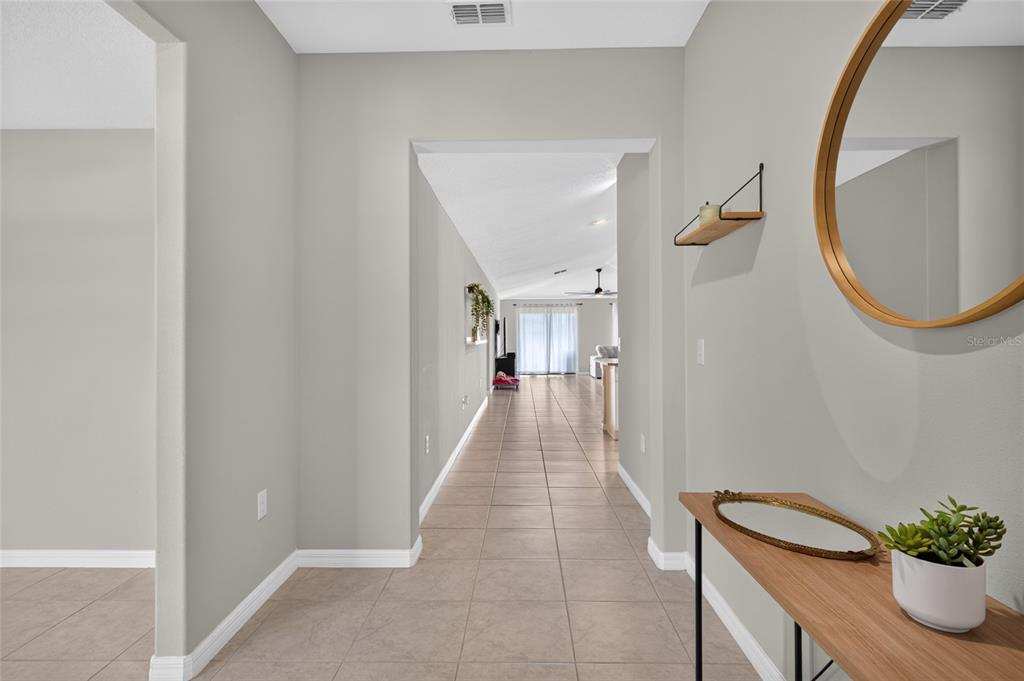 A tiled hallway leads from a foyer toward a bright living area with glass doors — 5420 LESLIE CANYON DRIVE, WIMAUMA, FL